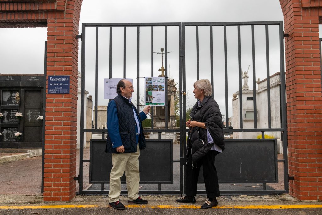 La alcaldesa y el responsable de Funcantabria observan el cartel anunciador de la actividad frente al cementerio de Polanco