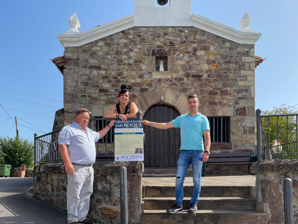 El concejal de Festejos, Fernando Sañudo (primero por la izquierda), sostiene el cartel de la fiestas de Posadillo junto a la ermita del pueblo, acompañado de los concejales Isabel Herrera y David Esteban