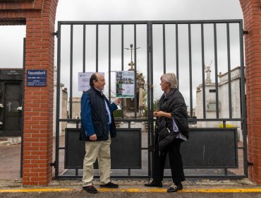 La alcaldesa y el responsable de Funcantabria observan el cartel anunciador de la actividad frente al cementerio de Polanco