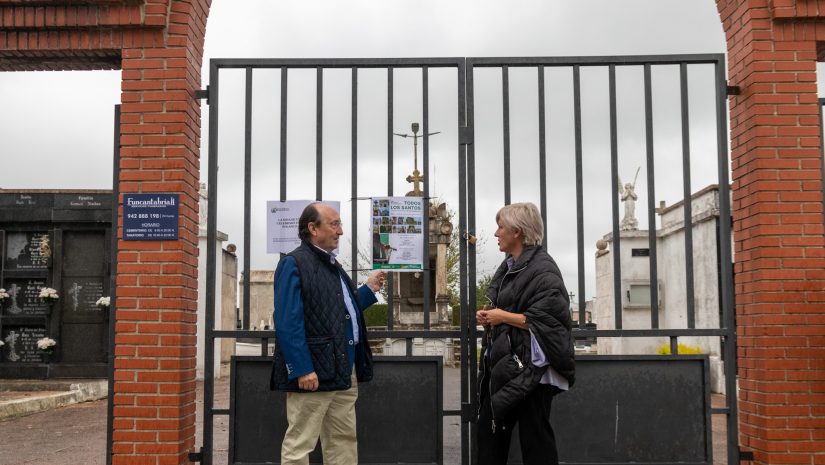 La alcaldesa y el responsable de Funcantabria observan el cartel anunciador de la actividad frente al cementerio de Polanco