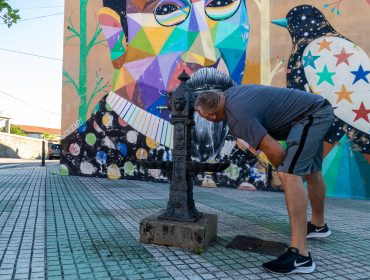Un vecino de Polanco bebe agua en la fuente pública situada junto al mural de Okuda