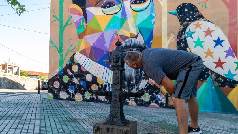 Un vecino de Polanco bebe agua en la fuente pública situada junto al mural de Okuda