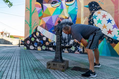 Un vecino de Polanco bebe agua en la fuente pública situada junto al mural de Okuda