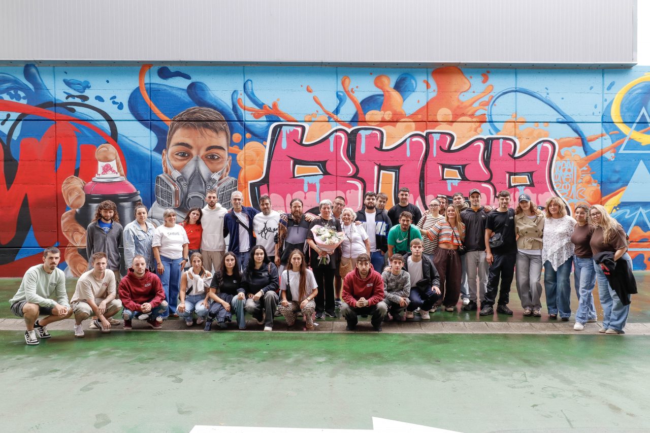 Familias, jóvenes y alcaldesa ante los dos elementos simbólicos del mural: un gran retrato realista de Carlos durante la realización de una pintada artística y su firma “Posa”
